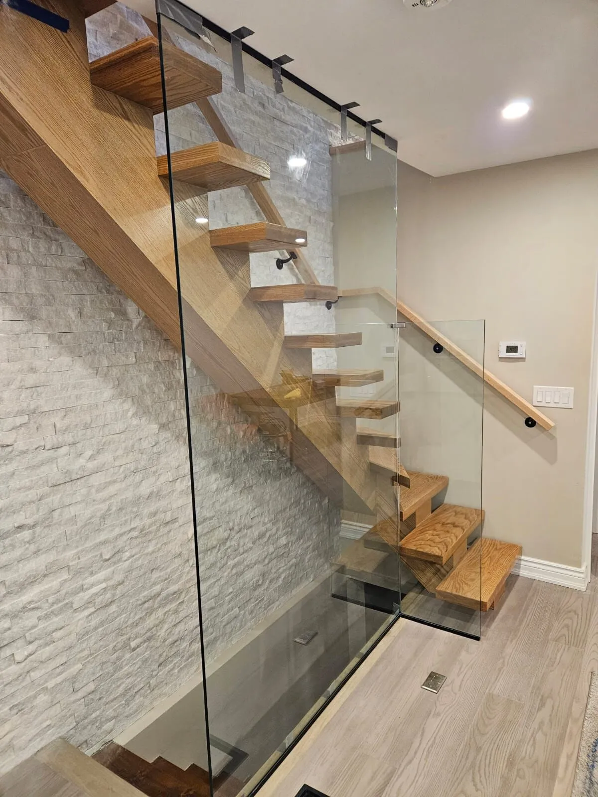 Floating oak staircase with glass railing and stone feature wall, built by EH Contracting